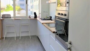 A modern kitchen with a built-in oven, a window with a view of buildings, and two white chairs. - Madeira, 3 bedroom apartment w Ocean Views Funchal (Funchal)