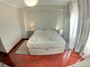 Un dormitorio con cama, mesitas de noche, una lámpara y una ventana con cortinas.
