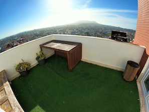 A rooftop terrace with artificial grass, a wooden bench, potted plants, and a view of a cityscape. - Sintra, T3 duplex with magnificent views and balcony, Tapada das Mercês, Sintra (Algueirão)
