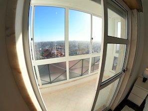 Une vue panoramique sâoffre Ă travers une grande fenĂȘtre, dĂ©voilant un paysage urbain avec des bĂątiments et un ciel dĂ©gagĂ©.