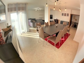 Un espace de salle Ă manger moderne avec une grande table et des chaises, un tapis rouge et une cuisine en arriĂšre-plan.