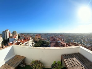 Une terrasse sur le toit offrant une vue sur le paysage urbain, avec des bùtiments et un ciel dégagé.