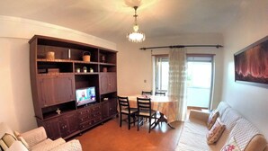 Una sala de estar con televisor, sofá, sillones, una mesa de comedor y un mueble de madera grande.