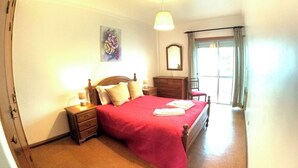 Un dormitorio con cama, mesitas de noche, cómoda, espejo y un cuadro en la pared.