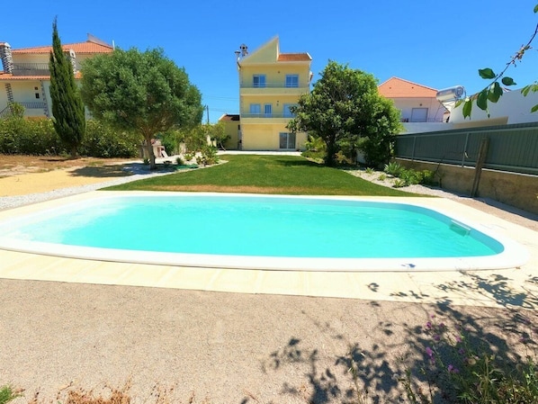A swimming pool with a surrounding patio area, a multi-story building in the background, and a clear blue sky.