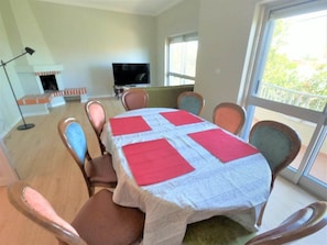 A dining area with a table set for six, surrounded by chairs, a fireplace, a television, and a large window.