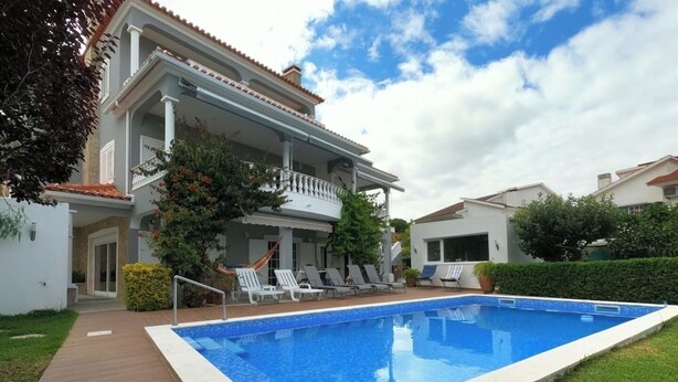 Une maison à deux étages avec une piscine, un patio couvert doté de chaises longues et un jardin bien entretenu.