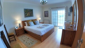 Une chambre à coucher comprenant un lit, des tables de chevet, une chaise, un tapis, une commode, un miroir et un lustre.