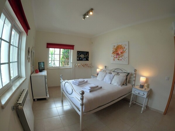 A bedroom with a bed, bedside tables, a radiator, a window with a view, and artwork on the wall.