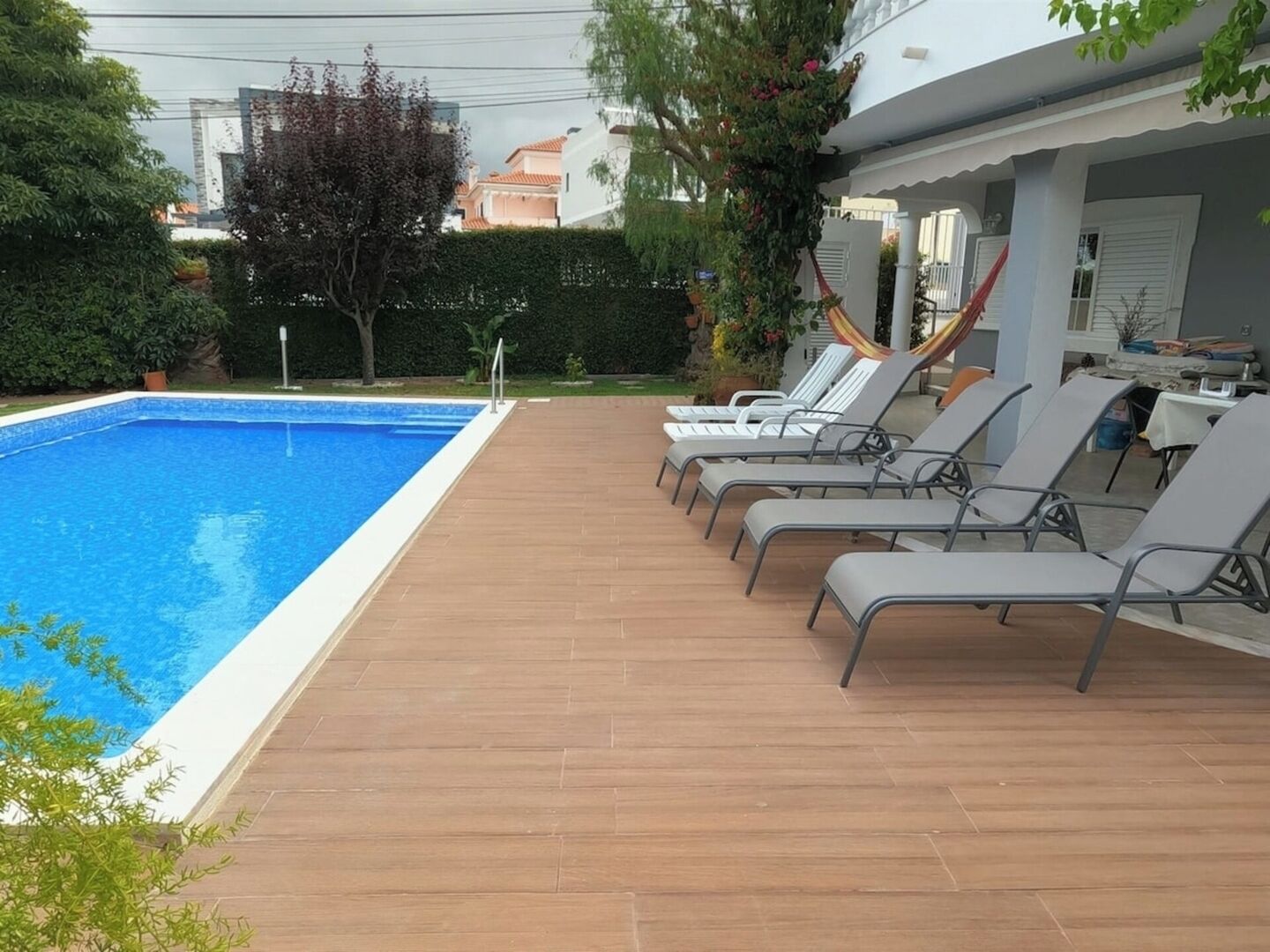 Una piscina con sillas de descanso, una hamaca y vistas de edificios al fondo.