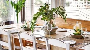 A dining area with a table set for four, featuring a vase with green foliage, candles, and wine glasses. - Akti Retzika (Thermaikos)