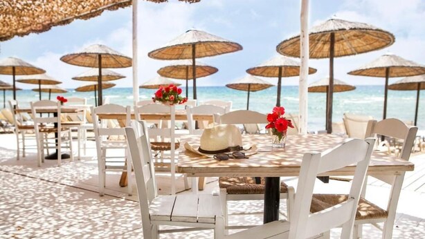 A beachside restaurant with white chairs and tables, straw umbrellas, and a view of the ocean. - Akti Retzika (Thermaikos)