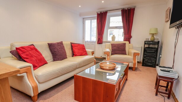 A living room with a beige sofa, red and brown cushions, a glass coffee table, a wooden side table, a television, and a DVD player. - Bronte Cottage (Keighley)