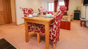 A dining area with a wooden table set for four, surrounded by floral-patterned chairs. - Bronte Cottage (Keighley)