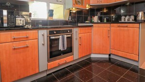 A modern kitchen with wooden cabinets, a built-in oven, a microwave, and a window with a view. - Bronte Cottage (Keighley)