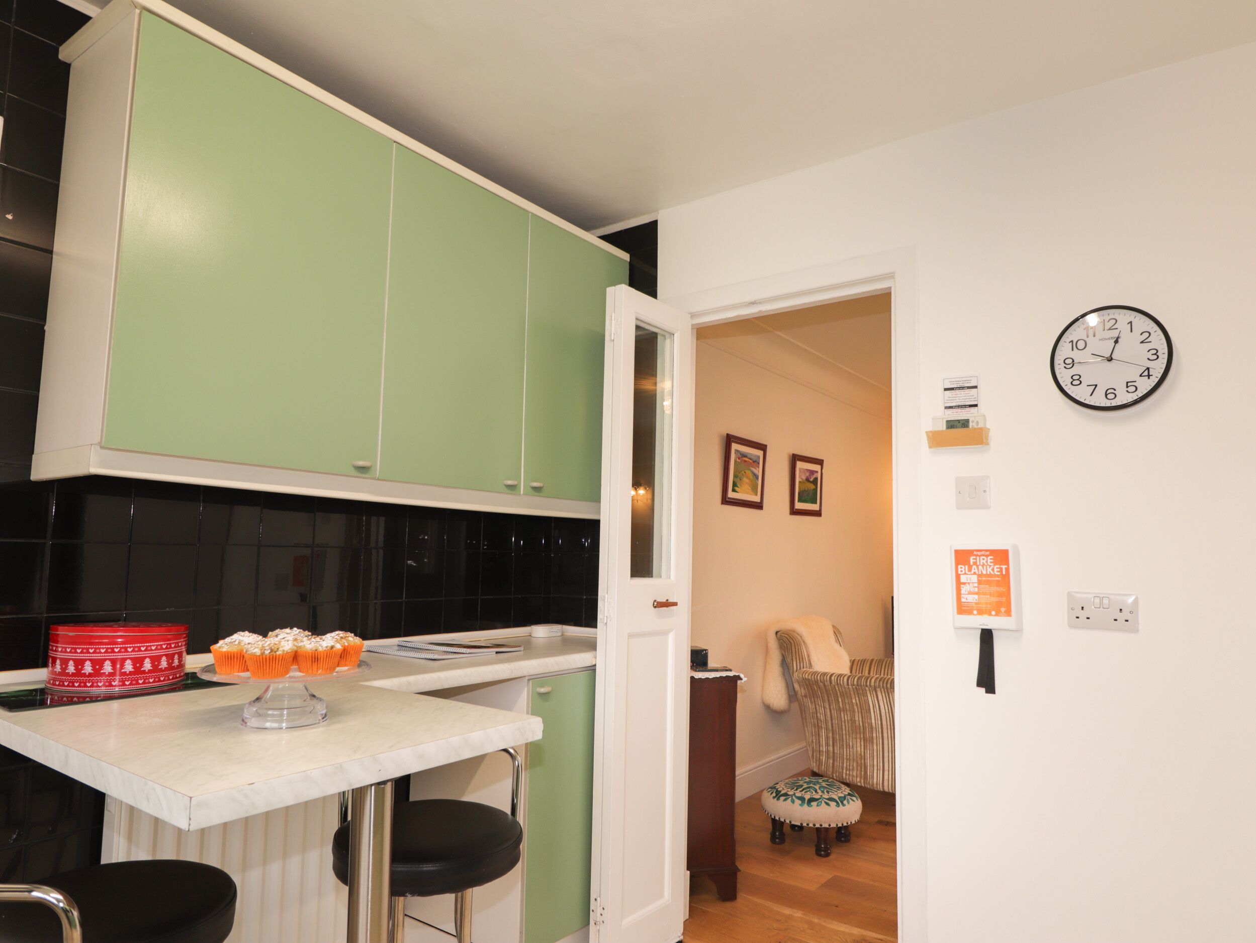 A kitchen with green cabinets, a white countertop, and a clock on the wall.