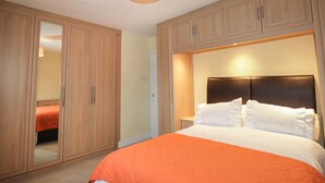 A bedroom with a large bed, wooden wardrobe, and a mirror.