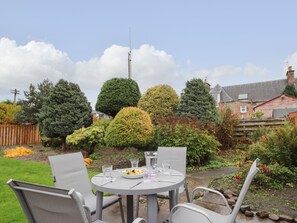 A round table with four chairs in a garden setting, surrounded by various trees and a wooden fence. - Tommy's (Inverness)