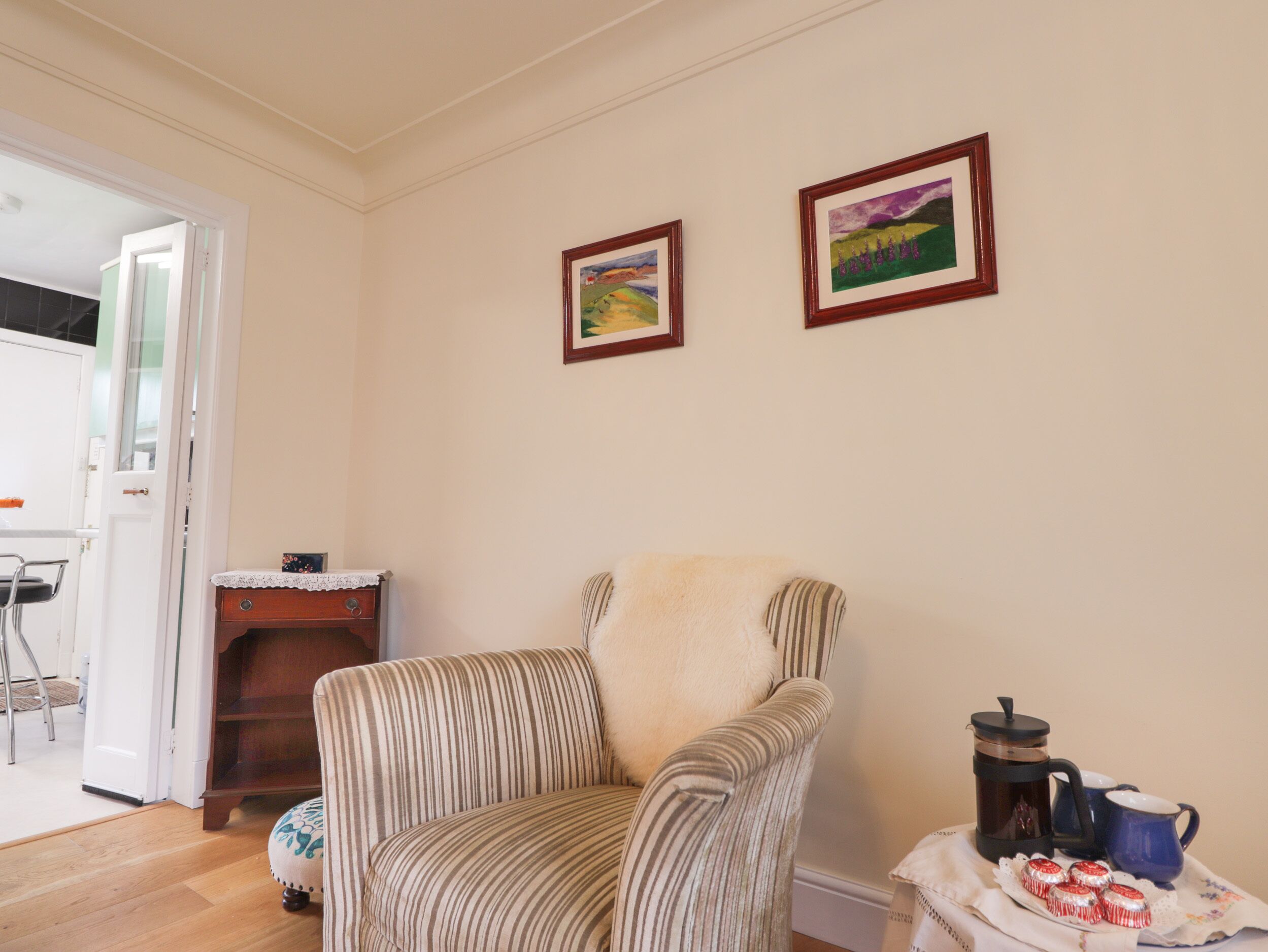 A striped armchair with a cushion, a small table with a coffee maker and cups, and two framed paintings on the wall.
