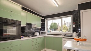 A modern kitchen with green cabinets, a black oven, a microwave, and a sink.
