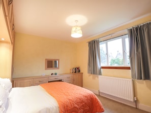 Une chambre à coucher avec un lit, une commode, un miroir et une fenêtre avec des rideaux.