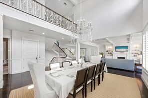 Un comedor espacioso con candelabro, paredes blancas y una escalera que conduce a un nivel superior.