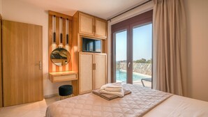 A hotel room with a bed, a television, a large window with a view of a pool, and a wooden wardrobe. - Pool Villa close to Elafonisi (Kissamos)