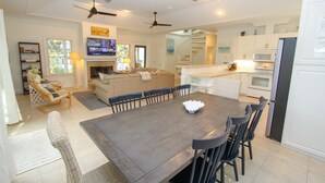 A spacious living room with a dark wooden dining table, a beige sofa, and a television. - L'escapade, Old Seagrove, Near Seaside, Private Heated Pool, Close to Beach (Seagrove Beach)