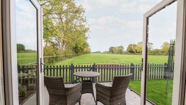 Un patio con mobiliario de mimbre y vista a un campo verde a través de una valla de madera.