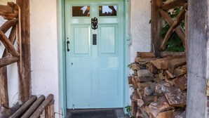Une porte vert clair avec un heurtoir en métal, une petite fenêtre au-dessus et un mur de pierre sur la droite.