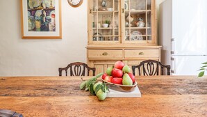 Un coin repas comprenant une table en bois, des chaises, un panier de fruits, une horloge et un meuble avec des portes en verre.