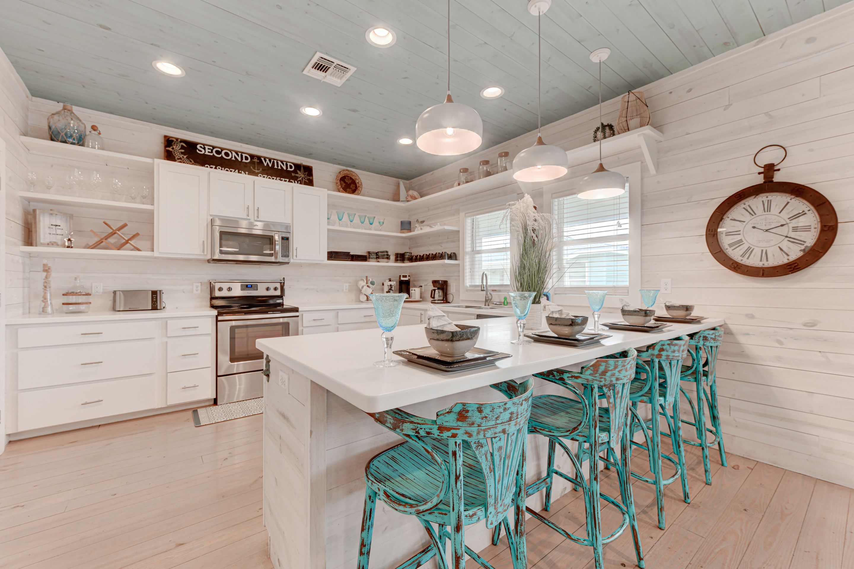 A kitchen with white cabinets, a central island, teal chairs, and a wall clock.