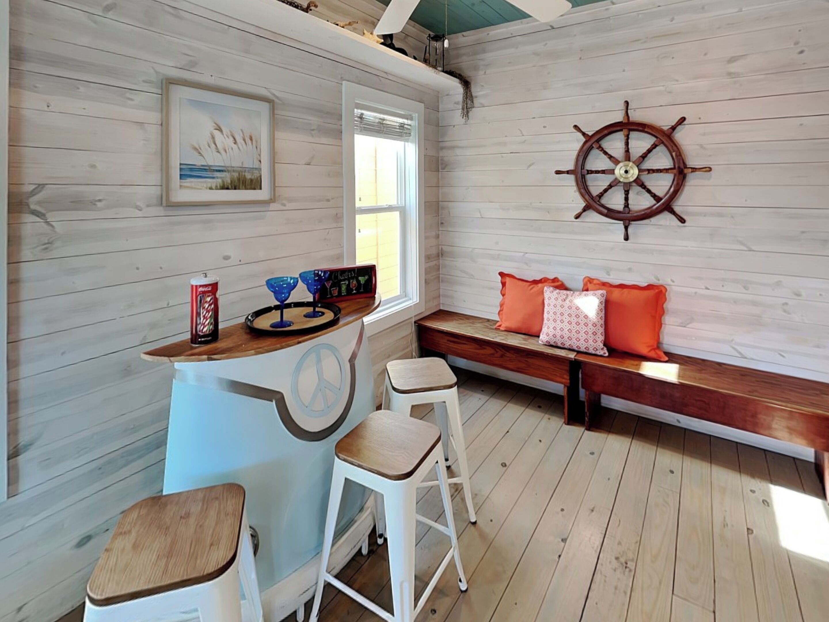 Een gezellige kamer met een houten bar, een grote decoratie van een scheepsschijf, een bank met kussens en een lijst met een afbeelding aan de muur.