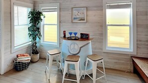 Une pièce chaleureuse avec un plancher en bois, une table ronde ornée d’un symbole de paix, trois tabourets blancs, une plante en pot et un tableau encadré accroché au mur.