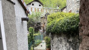 Ein schmaler Steinweg führt zu einem rustikalen Gebäude mit einer Holztür und einem Metallgitter.