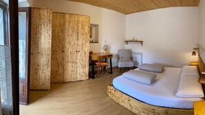 Ein gemütliches Zimmer mit einem Bett, einem Sessel, einem kleinen Tisch und einem Holzschrank.