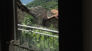 Blick aus einem Fenster auf eine gebirgige Landschaft mit einem Steinhaus und einem Gebäude mit rotem Dach.
