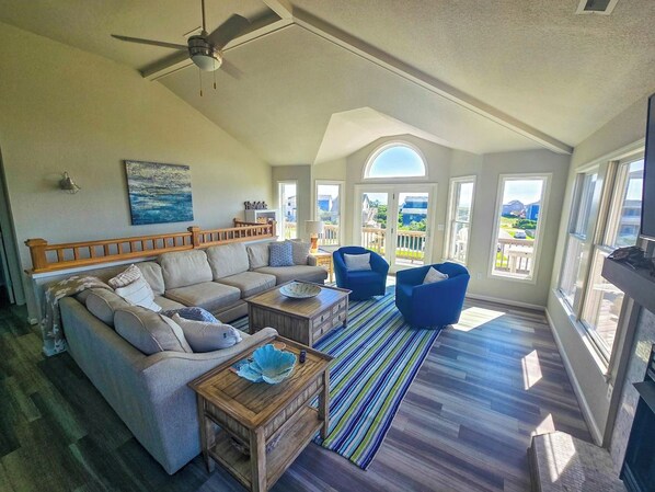 A spacious living room with a high ceiling, a ceiling fan, a large window, and a view of the outdoors.