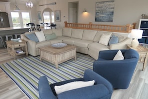 A living room with a large beige sectional sofa, a blue armchair, a wooden coffee table, and a striped rug.