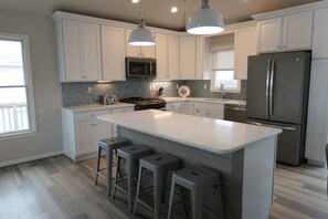 A modern kitchen with white cabinets, a central island with bar stools, stainless steel appliances, and pendant lighting.