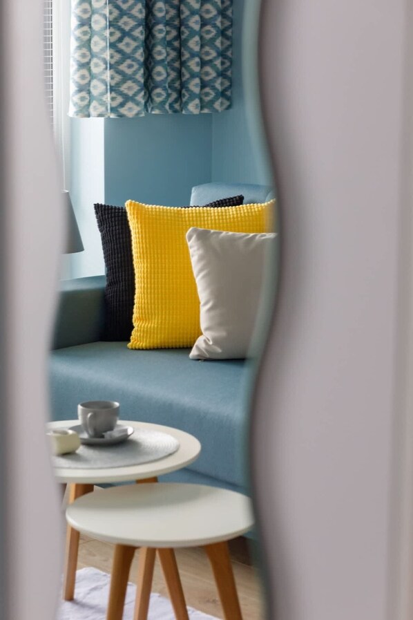 Una sala de estar moderna con un sofá azul, cojines amarillos y negros, y una pequeña mesa redonda con una taza y un platillo.