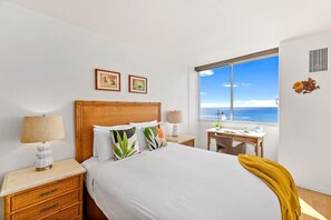 Un dormitorio con cama, mesitas de noche, un escritorio y una ventana con vista al mar.