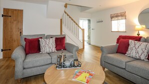 A living room with two grey sofas, red and floral cushions, a coffee table with a magazine, and a wooden door. - Hen Felin (Pwllheli)