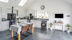 A modern kitchen with white cabinets, a dining area with a table and chairs, a washing machine, and a TV mounted on the wall. - Hen Felin (Pwllheli)