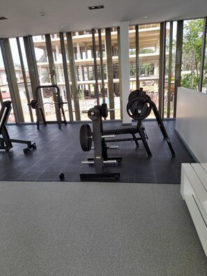 Une salle de sport équipée de matériel de musculation, dotée de grandes fenêtres et offrant une vue sur un bâtiment à l’extérieur.