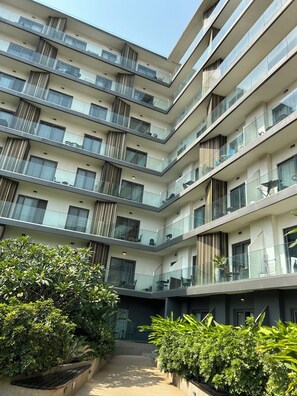 A multi-story residential building with balconies, large windows, and a central courtyard with greenery. - Lennox 1bed (Accra)