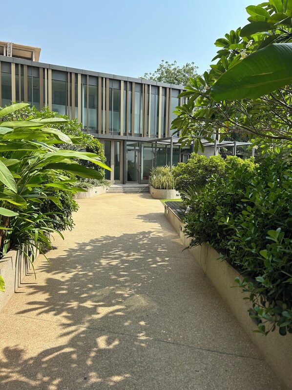 A modern building with a glass entrance, surrounded by well-maintained greenery and a paved walkway.