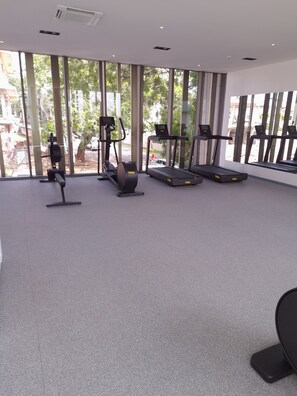 Une salle de sport équipée de tapis de course, d’un vélo elliptique et d’un vélo d’appartement, avec de grandes fenêtres et un sol recouvert d’un tapis gris.