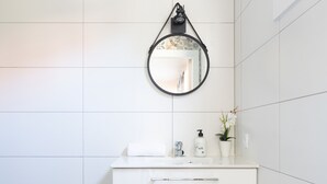 A modern bathroom with white tiles, a white vanity with a mirror, and a brown rug. - Las Latas del Almendro 1 (Santiago del Teide)