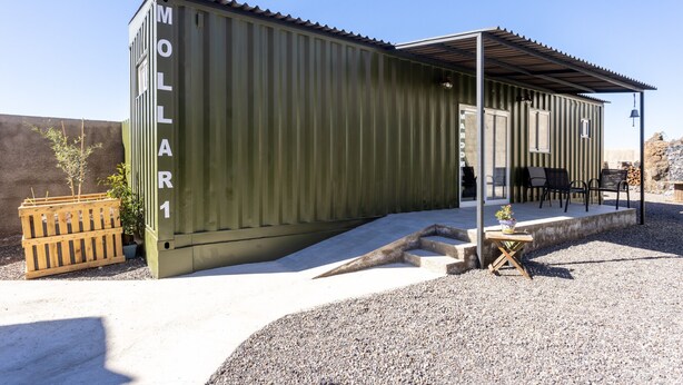 A green shipping container converted into a small building with a patio area, outdoor seating, and a bell. - Las Latas del Almendro 1 (Santiago del Teide)